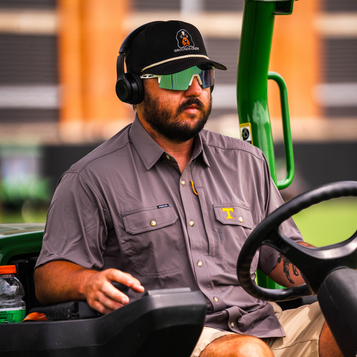 Man wearing The Bluetick shirt paired with sunglasses and headphones, seated outdoors on a utility vehicle.