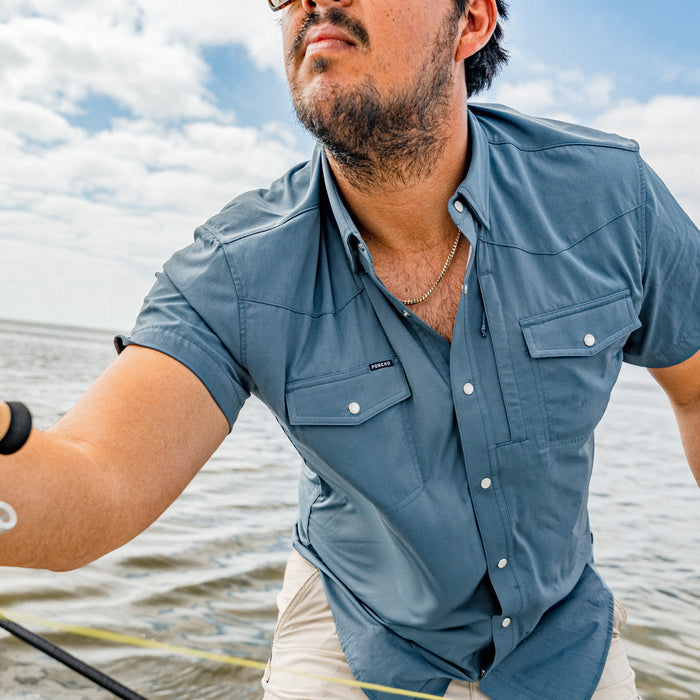 Man wearing The Dogtooth blue outdoor shirt with rolled sleeves near water