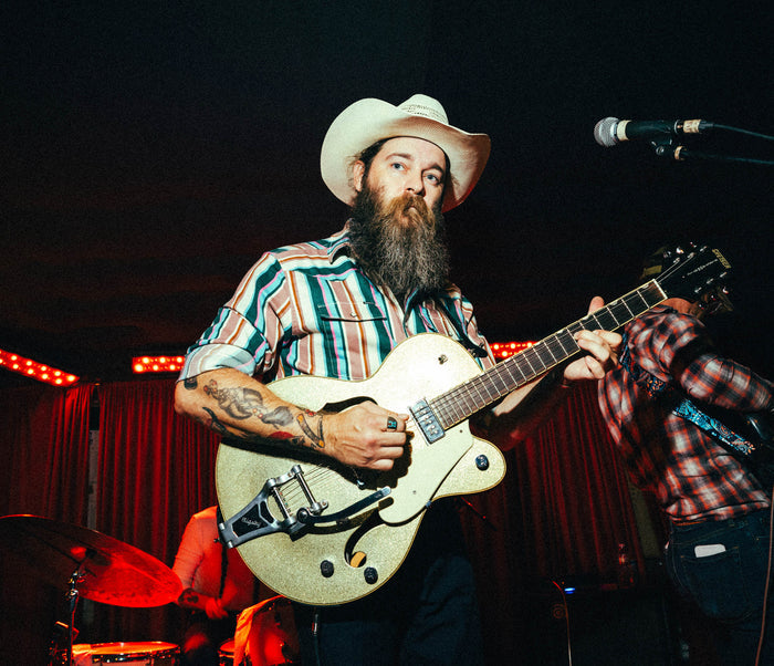 Man wearing The Frontman striped shirt and cowboy hat playing electric guitar on stage