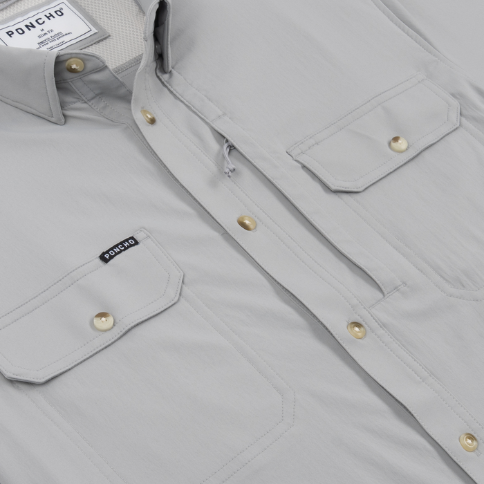 Close-up of a light grey outdoors shirt with brass buttons and pocket flaps, called The Grey Ghost.