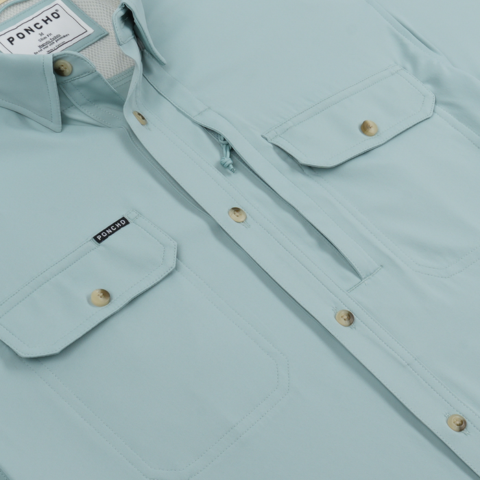Close-up of a light blue outdoor shirt with buttoned chest pockets and a Poncho label on one pocket.