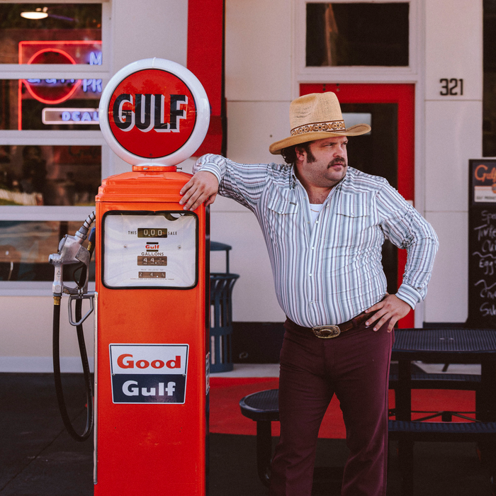 The Hammer Down shirt shown on a man in a cowboy hat beside a vintage gas pump