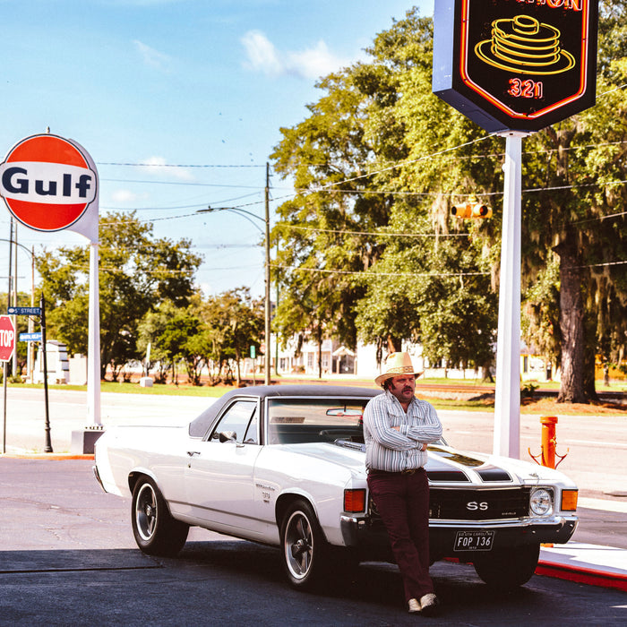 The Hammer Down shirt worn by a man beside a vintage white pickup at a roadside service station