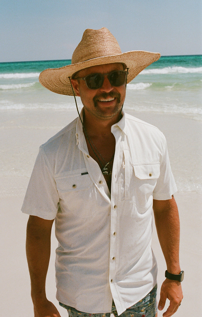 Man wearing The Key West white shirt with straw hat and sunglasses at the beach