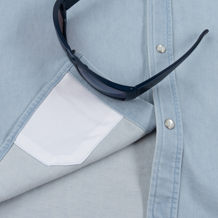 Close-up of light blue The Marfa shirt with white inner pocket and dark sunglasses resting on the fabric