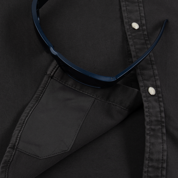 Close-up of a black button-up shirt pocket with sunglasses resting on The Matamoros shirt fabric.