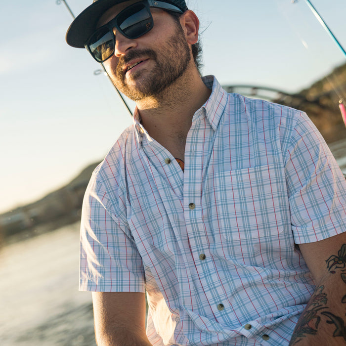 Man wearing The Mullet short-sleeve plaid outdoor shirt by water with sunglasses and hat