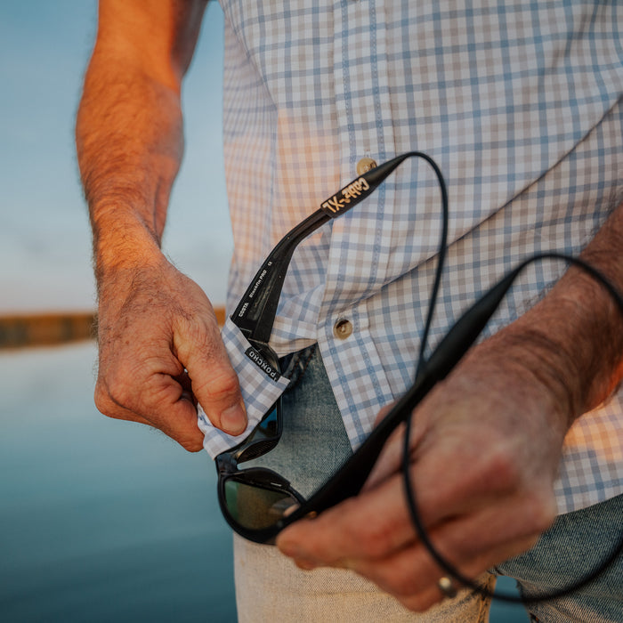 cleaning sunglasses in grey and blue plaid shirt