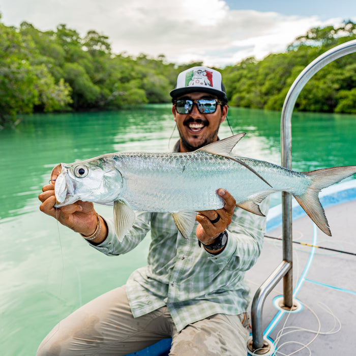 Man wearing The Sapelo outdoor shirt holding a large silver fish on a boat in clear green water