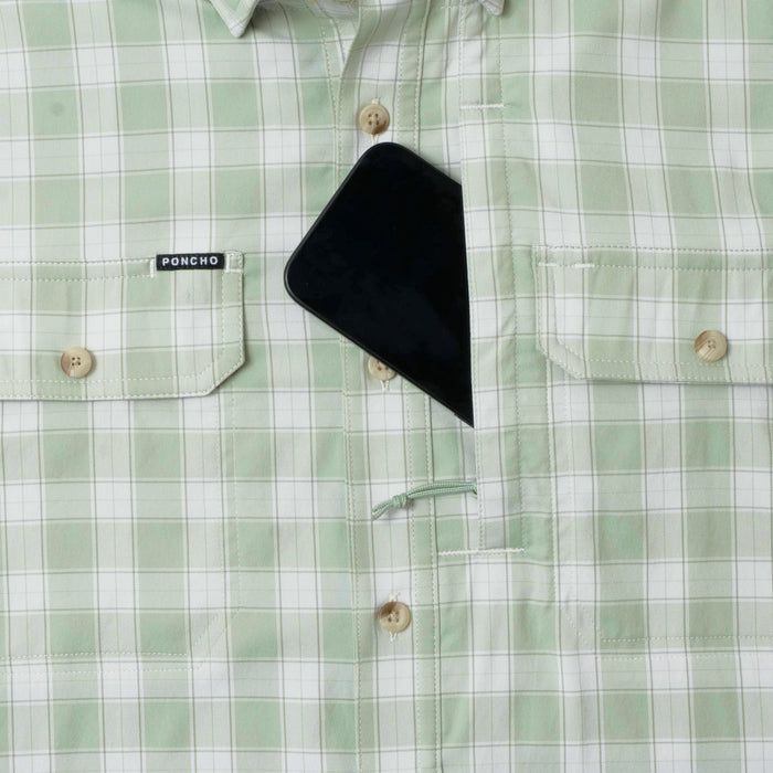 Close-up of green plaid button-up shirt with chest pockets and a phone partially tucked inside, featuring The Sapelo label.