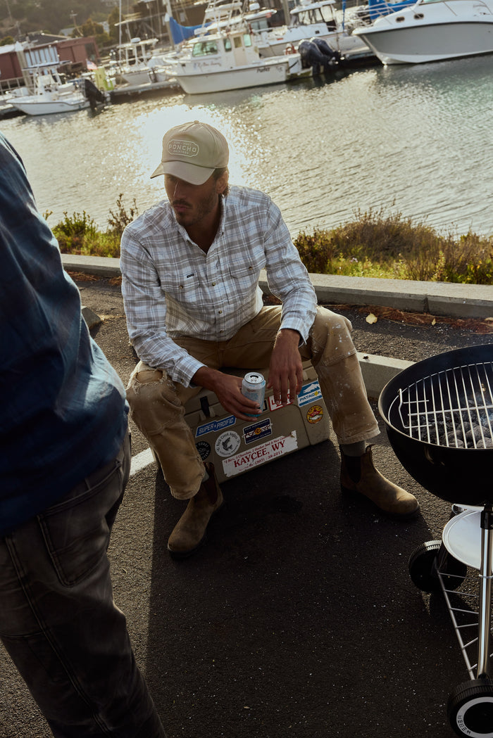 The Snowcat plaid shirt worn by a man seated beside a marina and barbecue grill