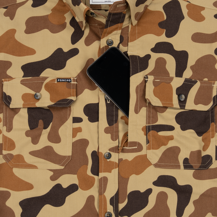 Close-up of The Stuttgart shirt in brown and tan camouflage pattern with front pockets and a black smartphone tucked inside one pocket.
