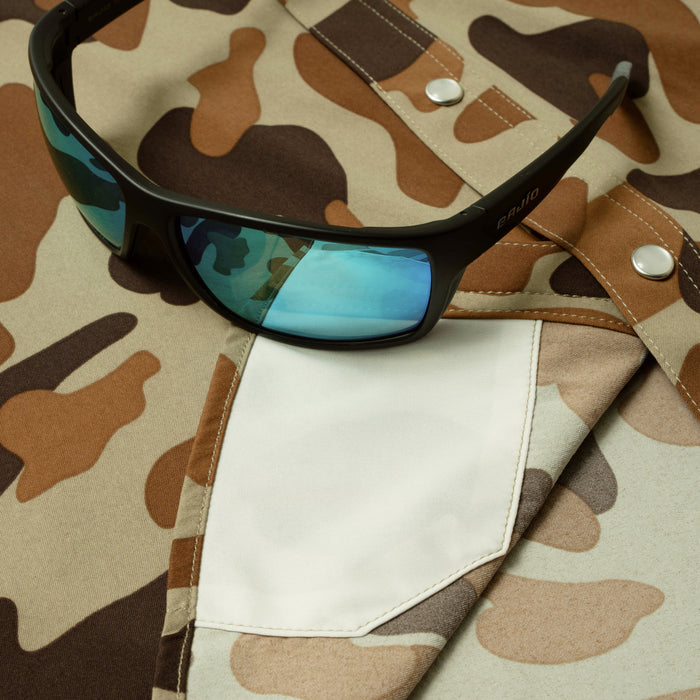 Black sunglasses with blue lenses resting on camo shirt pocket from The White Wing collection