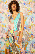 A woman wears the Tropical Fantasy Sleeveless Dress, featuring an abstract print, as she stands before a vibrant background with bold shapes and zebra-like stripes.