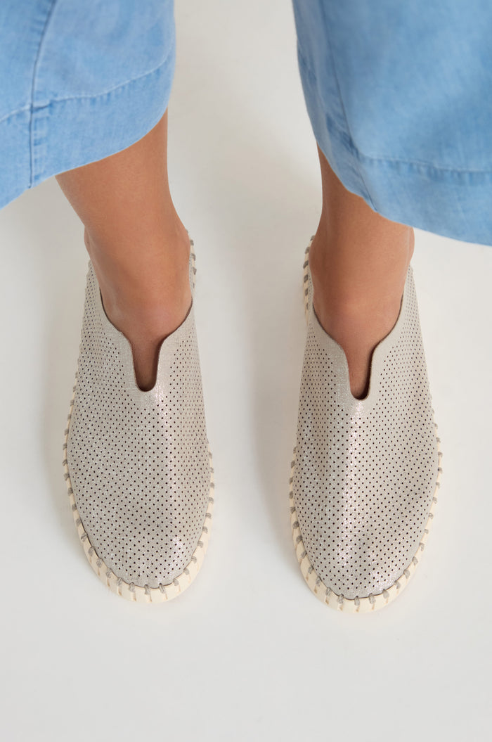 A person wearing light blue pants and Tulip Glimmer Platform Slip on Shoes is standing on a white surface.
