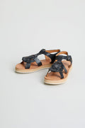 The Tulum Leather Sandals feature black leather woven straps, a buckle, and tan soles. Handcrafted by Mapache Tulum, they are shown on a plain white background.