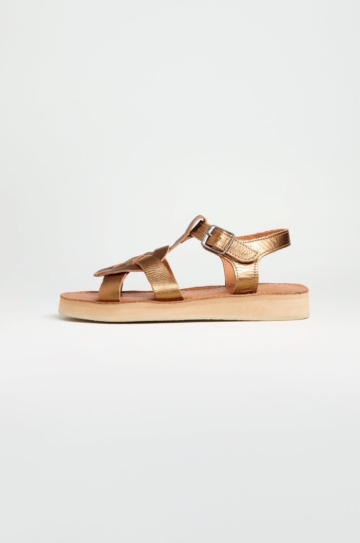 A single Tulum Leather Sandal in metallic gold leather with an open toe, buckle strap, and flat beige sole is shown in profile against a plain white background.