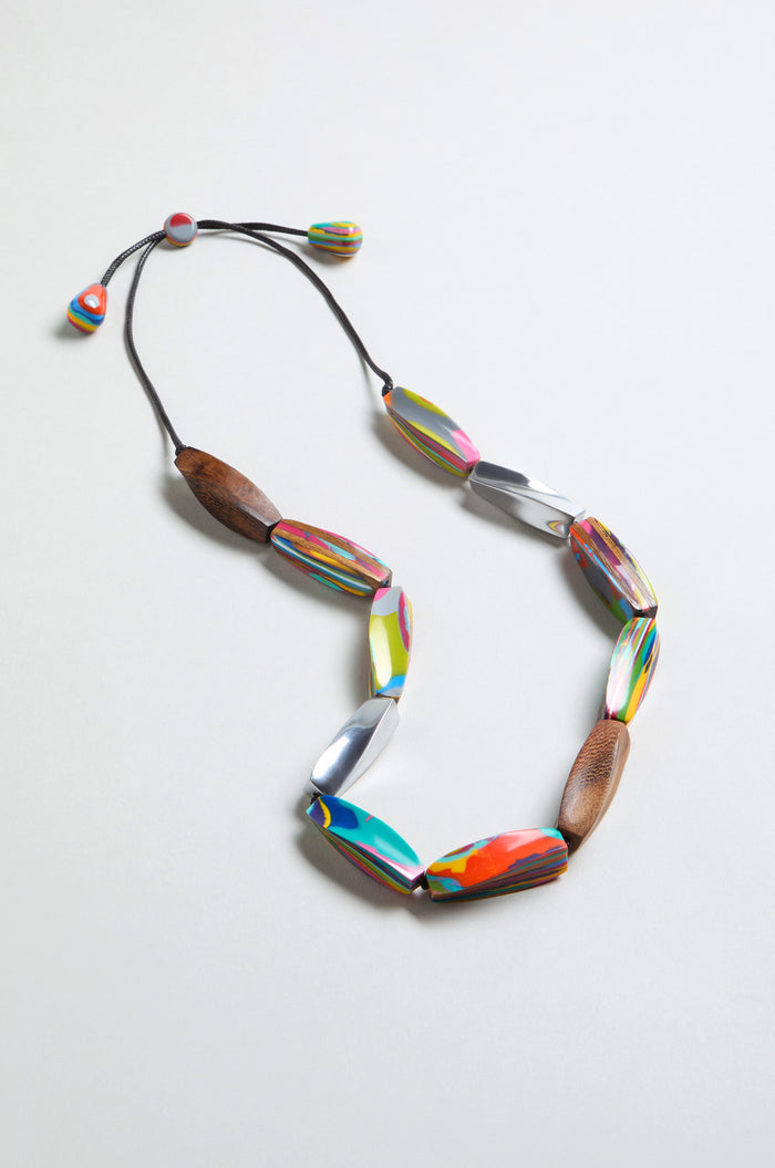 The Twisted Shapes Necklace showcases colorful oval beads and natural wood accents, set against a white background.
