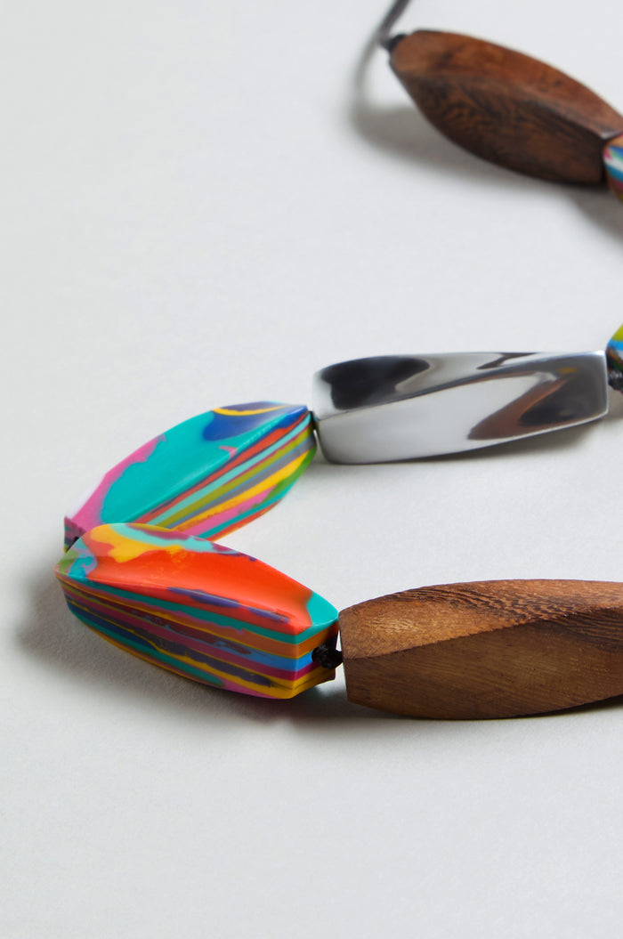Close-up of the Twisted Shapes Necklace with multicolored marbled beads, carved wooden beads, and recycled aluminum accents shown on a light background.
