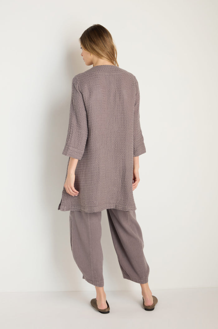 A woman faces away, wearing the Waffle Linen Long Jacket in textured mauve with matching wide-leg pants and flats, set against a plain white background.