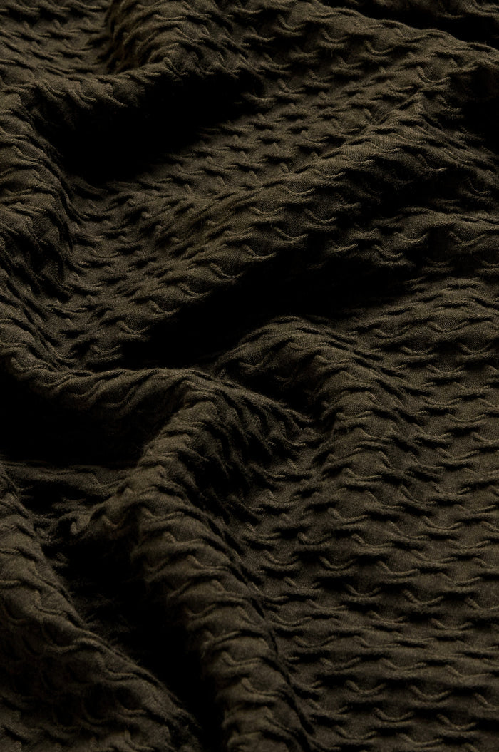 Close-up of the Waffle Textured Jersey Pine Cowl Neck Top, showcasing its dark, textured fabric with a wavy, crinkled pattern and raised dot-like details—folds and shadows highlight the unique waffle texture typical of this English-made design.