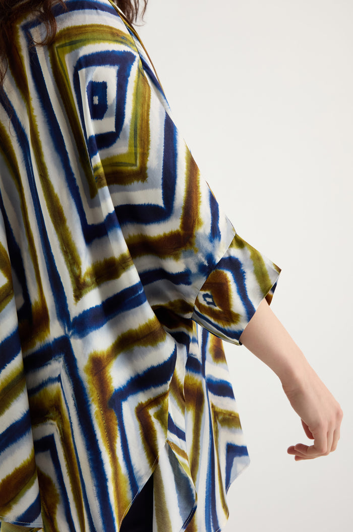 Someone wearing the Wavy Lines Print Shirt, featuring a loose fit and abstract blue, olive green, and white wavy lines pattern, extends their right arm.